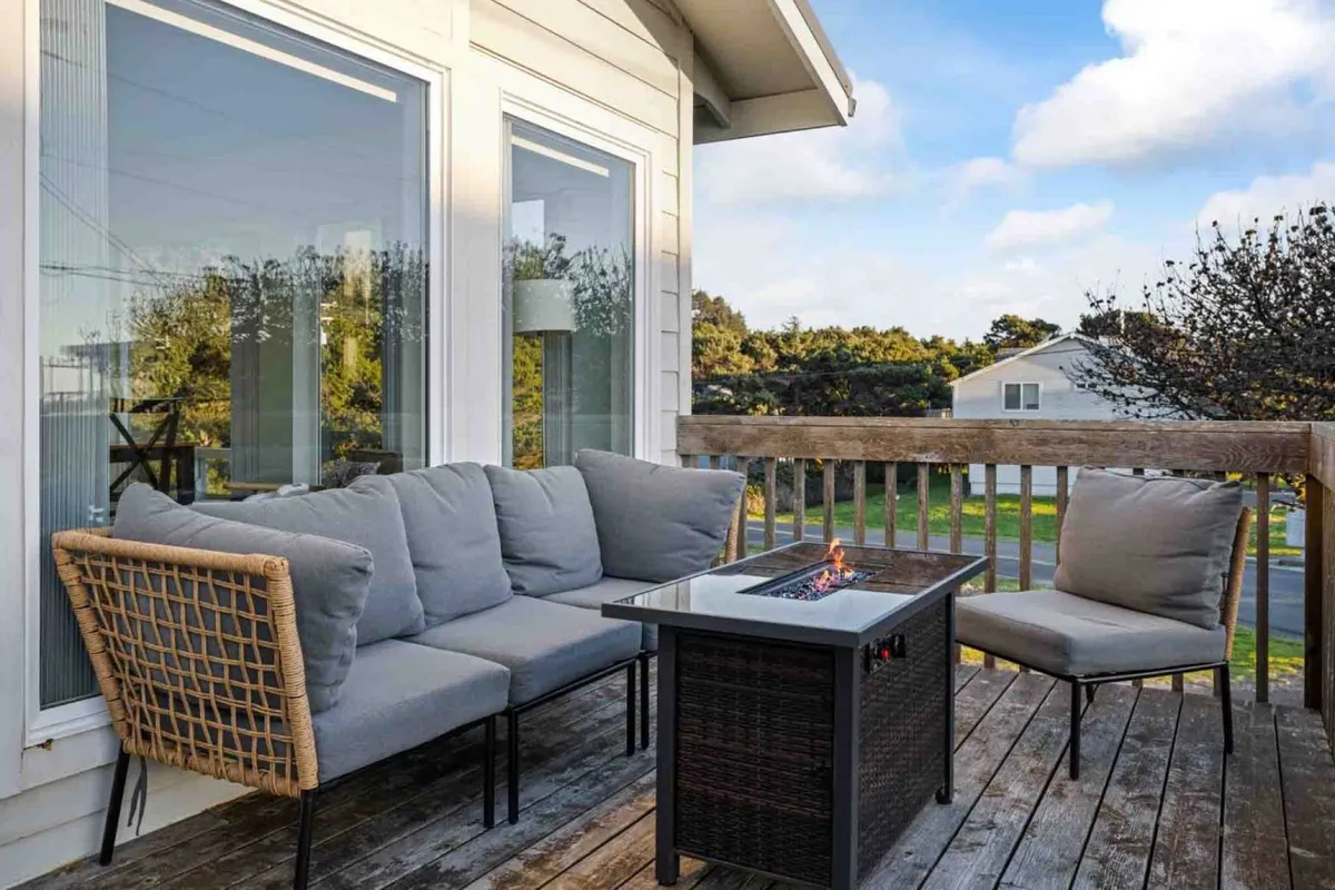 A cozy outdoor seating area with comfortable chairs and a fire pit, set against a backdrop of large windows overlooking lush greenery. The inviting space bridges the indoors and outdoors, ideal for relaxing after a lakeside or beach stroll with your pet.
