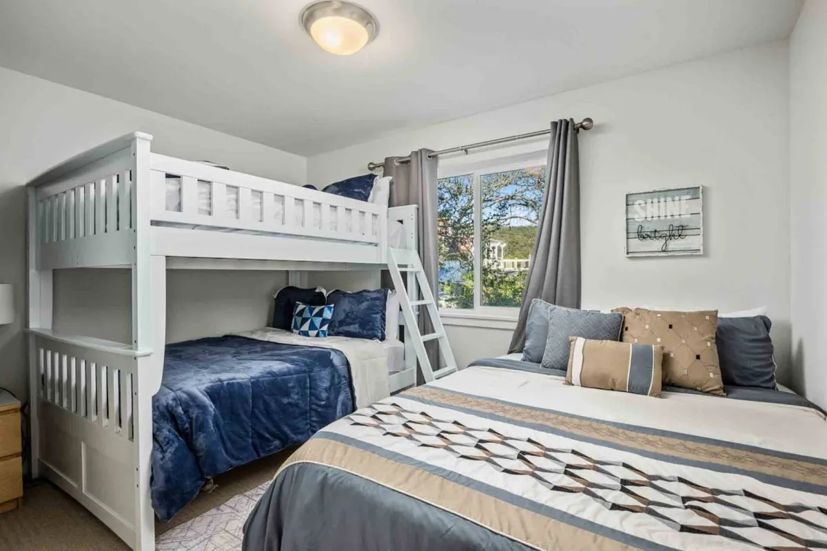 A cheerful lower-level bedroom with a bunk bed, a double bed, decorative pillows, wall art, and a window letting in natural light. The space feels cozy and playful, perfect for families or groups of friends.
