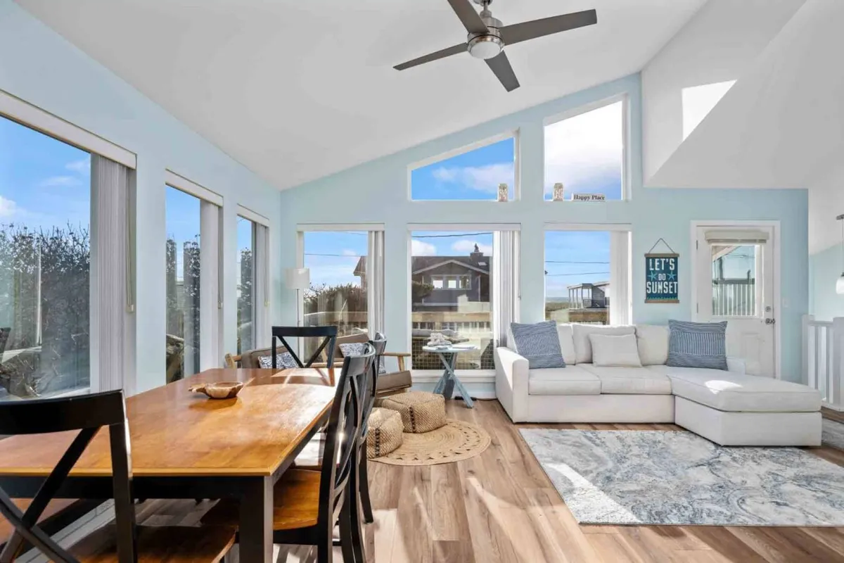 A cheerful, light-filled interior with a dining table and sofa positioned by large windows. Decorative touches and a bright, inviting atmosphere make this a perfect spot for family meals, social gatherings, or simply enjoying the sunset together.