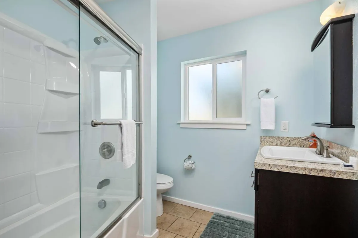 A bright, modern bathroom with a glass shower enclosure, sleek granite countertop, and a window letting in abundant natural light. The space feels clean and tranquil, offering a private retreat for relaxation.
