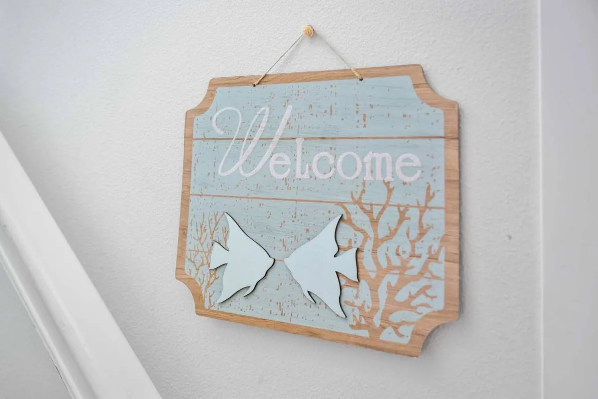 An inviting entryway featuring a friendly 'Welcome' sign, playful fish shapes, and coral-inspired decor. The space sets a warm, approachable tone for guests and hints at the home's relaxed, coastal atmosphere.