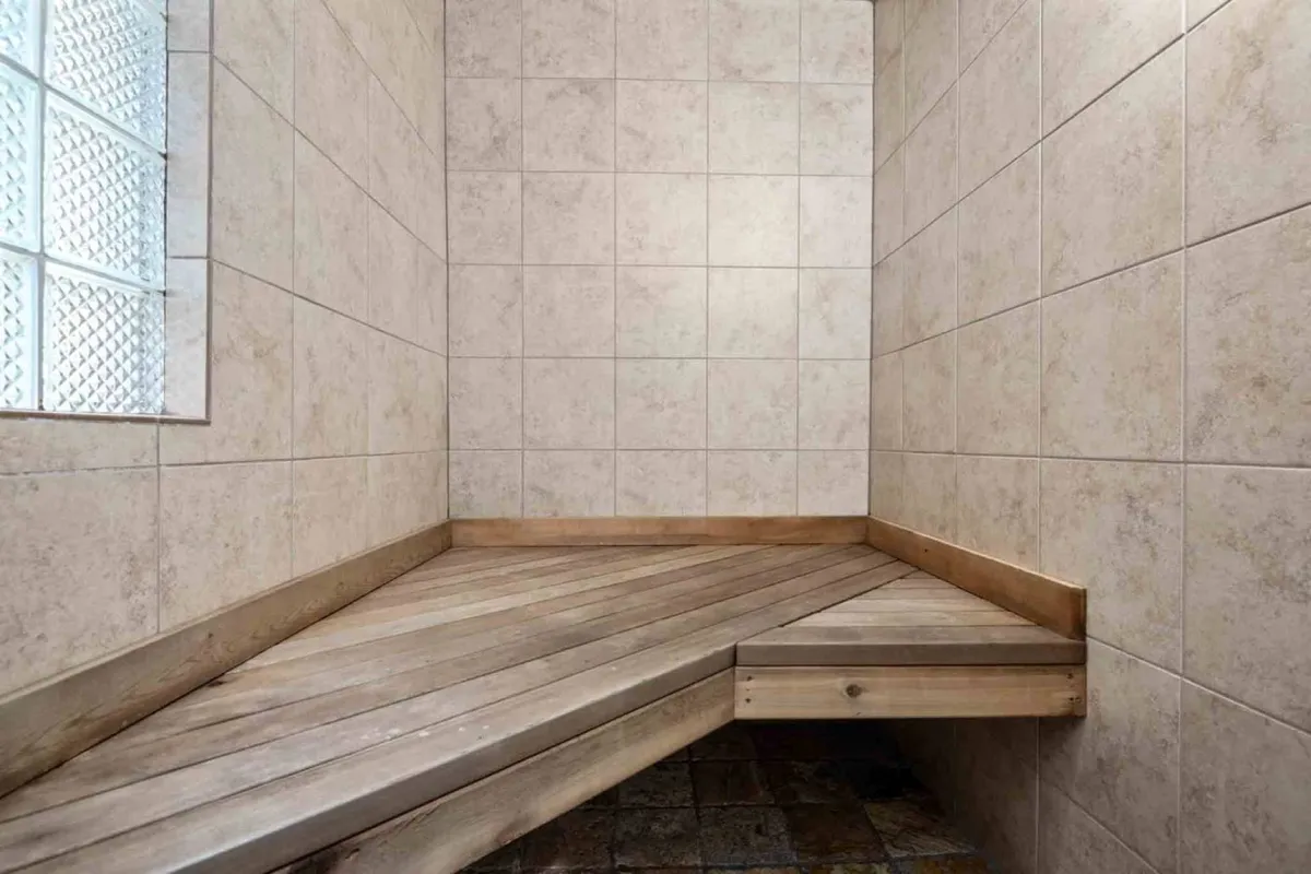 A spa-like bathroom featuring textured tile walls, a wooden bench, and a soft glow from a glass block window, creating an atmosphere of calm and relaxation ideal for self-care.